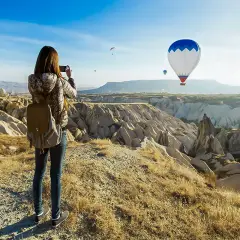 En kvinna med ryggsäck fotograferar den magiska vyn av luftballonger över Kappadokien, Turkiet.