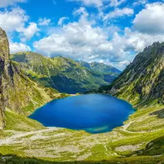 Blågrönt Morskie Oko, en sjö omgiven av gröna bergssluttningar och dramatiska klippor under en molnig himmel.