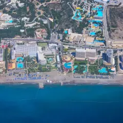 Vy från ovan över ett stort vattenland och hotellkomplex vid Rhodos kust. Solstolar och parasoller kantar stranden.