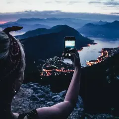 En person tar en bild med mobilen av en stad vid havet i Europa, med berg i bakgrunden.