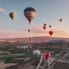 En magisk luftballong tur i Turkiet vid soluppgången. Många färgglada ballonger svävar över ett böljande landskap med byar och klippformationer.