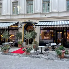 Elegant fasad med randiga markiser och utomhusbord. En röd matta leder till entrén till Dagmar restaurang.