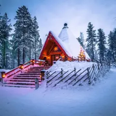 En snötäckt stuga i skogen, upplyst av julbelysning. En dröm för en solsemester vinter.