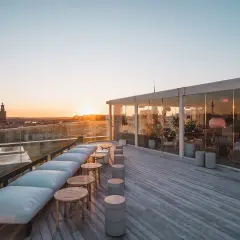 Takbar med utsikt över Stockholms silhuett vid solnedgången. En modern skyskrapa i Stockholm med sittplatser utomhus.