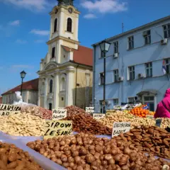 En marknad i Belgrad under en solig helg. Ett överflöd av nötter och torkad frukt säljs framför en kyrka och blå byggnad.