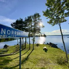 Vacker rastplats vid Norrbränningen, E4 norrut. Solen skiner över sjön, med picknickbord och en brygga.