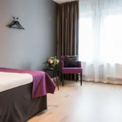 Ett hotellrum med en säng, en lila fåtölj och ett skrivbord. Perfekt för att sova på Arlanda.