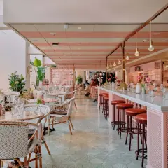 En ljus och luftig lokal med rosa och vita ränder i taket, som påminner om mysiga caféer i Stockholm. Vackra rottingmöbler och mycket gröna växter skapar en inbjudande atmosfär.