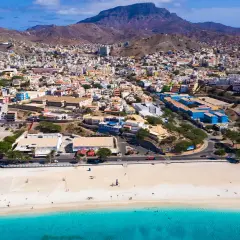 Färgstark stad i Kap Verde med en strand och turkost vatten. Berg reser sig bakom den tätbebyggda staden.