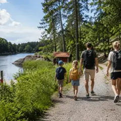 Familj vandrar längs en sjö, ett perfekt utflyktsmål i Stockholm. Barnen bär ryggsäckar, mamman en korg.
