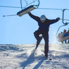 En skidåkare hoppar i luften på en snöig backe, med en skidlift i bakgrunden. Perfekt för skidorter i Dalarna!