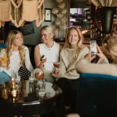 Tre unga kvinnor njuter av drinkar och sällskap under en mysig griffins brunch.