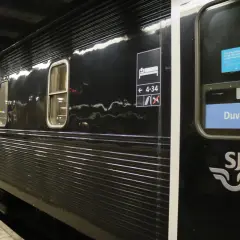 Svart liggvagn SJ vid perrongen. Vagn 14, Duved, med sovande symbol och nummer.