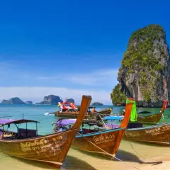Träbåtar guppar i det turkosa vattnet vid Koh Hong. En imponerande klippa reser sig ur havet.