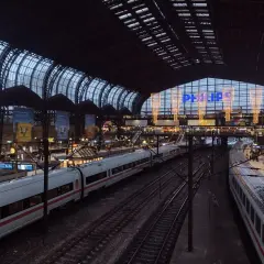 Tågstation med flera spår och vita tåg. En stor glas- och stålkonstruktion täcker taket. Philips-logotypen lyser i blått. Det är ett sj tåg till Hamburg.