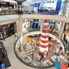 Inne i Terminal 21 Bangkok, ett shoppingcenter med flera våningar, syns en stor rödvit fyr i mitten. Folk shoppar och rör sig mellan butiker som Victoria's Secret.