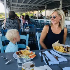 Familj njuter av en måltid på Costas Kitchen Kallithea. En kvinna ler, en pojke äter, och maten ser utsökt ut.