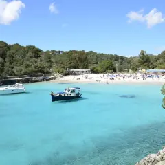 En solig dag på mallis Mallorca. Turkosblått vatten, en vit yacht och en blåvit båt i en vik med en livlig strand.