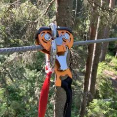 Nära en zipline i Umeå, en orange vajerklämma med röda och svarta band hänger redo för äventyr i skogen.