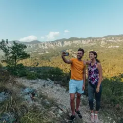 Ett par tar en selfie under sin vandring i Kroatien, med en fantastisk utsikt över berg och grönska.