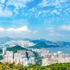 Vy över Hong Kongs tätbefolkade kustlinje med berg i bakgrunden och en blå himmel med moln.