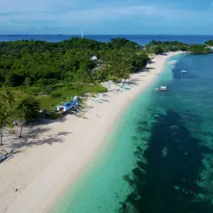 En vit sandstrand med palmer och traditionella filippinska båtar. Vattnet är turkost och klart, med en grönskande ö i bakgrunden. En idyllisk vy från Cebu, Filippinerna.