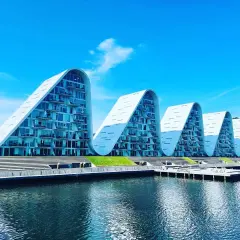 Vågformade byggnader vid vattnet i Vejle, Danmark. Moderna lägenheter med glasfasader och balkonger.