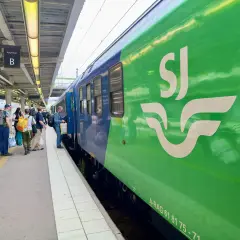 Folk väntar på perrongen vid ett grönt SJ-tåg, redo för en resa. Kanske är det ett tåg till London?