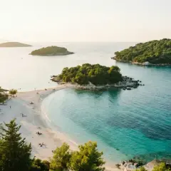 Vacker strand med turkost vatten och gröna öar. Perfekt för en resa till Albanien med tips om sol och bad.