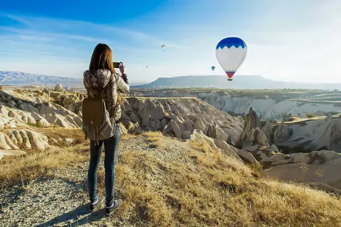 En kvinna med ryggsäck fotograferar den magiska vyn av luftballonger över Kappadokien, Turkiet.