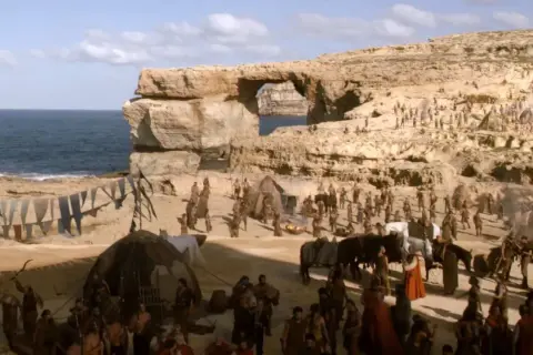 En scen från Game of Thrones på Malta, med en stor folkmassa och tält vid havet under en klippformation.