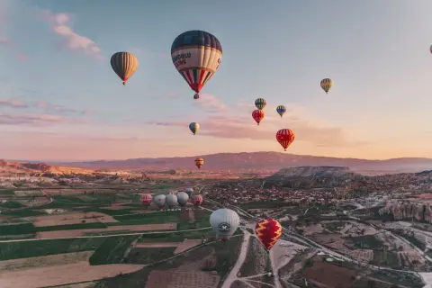 En magisk luftballong tur i Turkiet vid soluppgången. Många färgglada ballonger svävar över ett böljande landskap med byar och klippformationer.