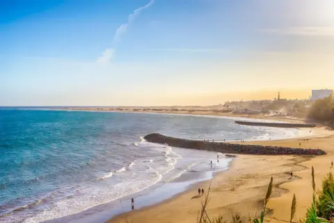 En vidsträckt gran canaria strand med turkost vatten, gyllene sand och några få besökare som njuter av solen.