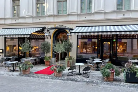 Elegant fasad med randiga markiser och utomhusbord. En röd matta leder till entrén till Dagmar restaurang.