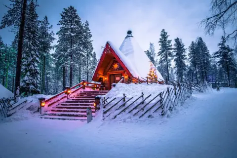 En snötäckt stuga i skogen, upplyst av julbelysning. En dröm för en solsemester vinter.