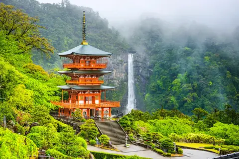 En orange pagod med gröna tak står vid en forsande vattenfall i en frodig, grön miljö. En del av Kumano Kodo-leden.
