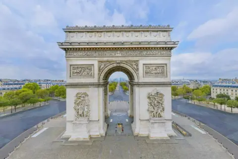 Paris's triumfbågen reser sig majestätiskt med sina detaljerade skulpturer. En tom Champs-Élysées sträcker sig mot horisonten under en molnig himmel.