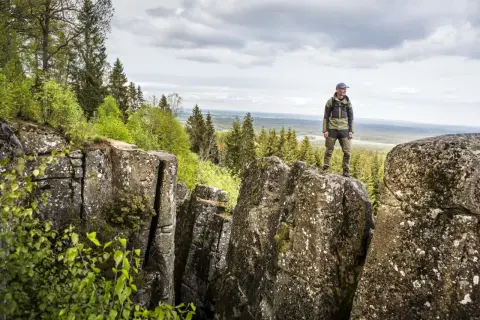 En man står på en klippa och njuter av utsikten över skog och landskap. En perfekt plats för att vandra i Europa.