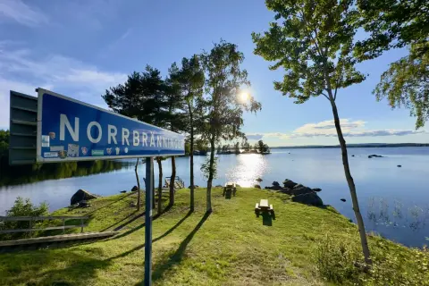 Vacker rastplats vid Norrbränningen, E4 norrut. Solen skiner över sjön, med picknickbord och en brygga.