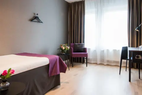 Ett hotellrum med en säng, en lila fåtölj och ett skrivbord. Perfekt för att sova på Arlanda.