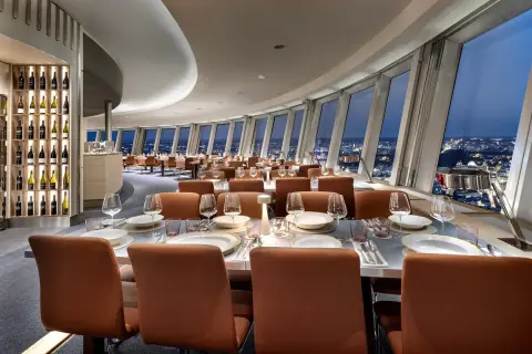 Elegant restaurang Berlin med utsikt över staden. Vackert dukade bord med glas och tallrikar. Vinhylla i bakgrunden.