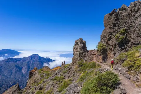 Vandrare på en bergstig med moln och berg i bakgrunden. Fantastiska vandringsleder på Gran Canaria.