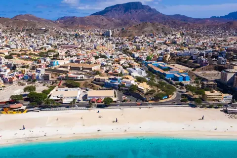 Färgstark stad i Kap Verde med en strand och turkost vatten. Berg reser sig bakom den tätbebyggda staden.