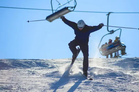 En skidåkare hoppar i luften på en snöig backe, med en skidlift i bakgrunden. Perfekt för skidorter i Dalarna!