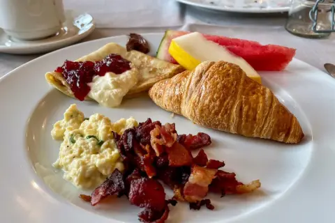 En härlig **continental frukost** med krämiga äggröror, knaprigt bacon, en croissant, pannkakor med sylt och grädde, samt färsk frukt.