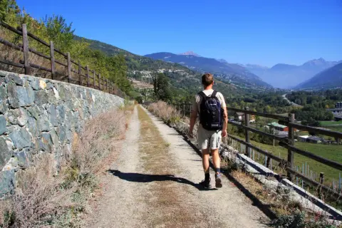 Man vandrar på en grusväg i Italien, med en stenmur till vänster och en vacker dal med berg i bakgrunden.
