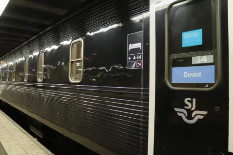 Svart liggvagn SJ vid perrongen. Vagn 14, Duved, med sovande symbol och nummer.