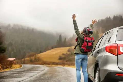 En person med ryggsäck vid en bil på en väg i Sverige. Vackert landskap med dimmiga berg. Bilsemester Sverige!