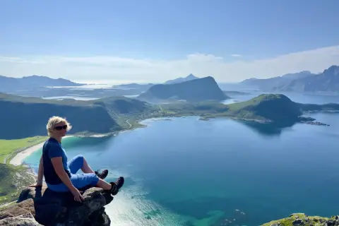 Kvinna sitter på klippavsats med fantastisk utsikt över fjordlandskap på Lofoten.