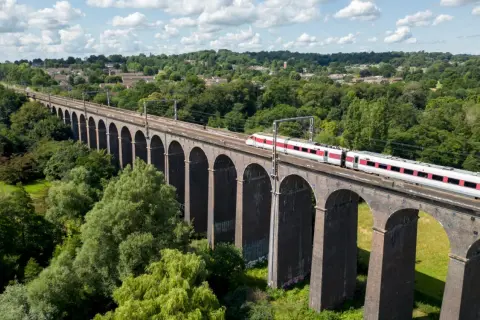 Ett modernt tåg susar fram över en gammal tegelbro, en perfekt bild för att tågluffa i England.